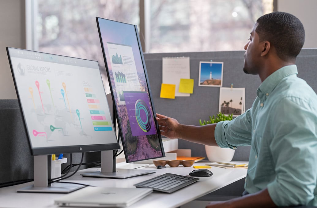 A business man in an office is checking reports on his two computer monitors.
