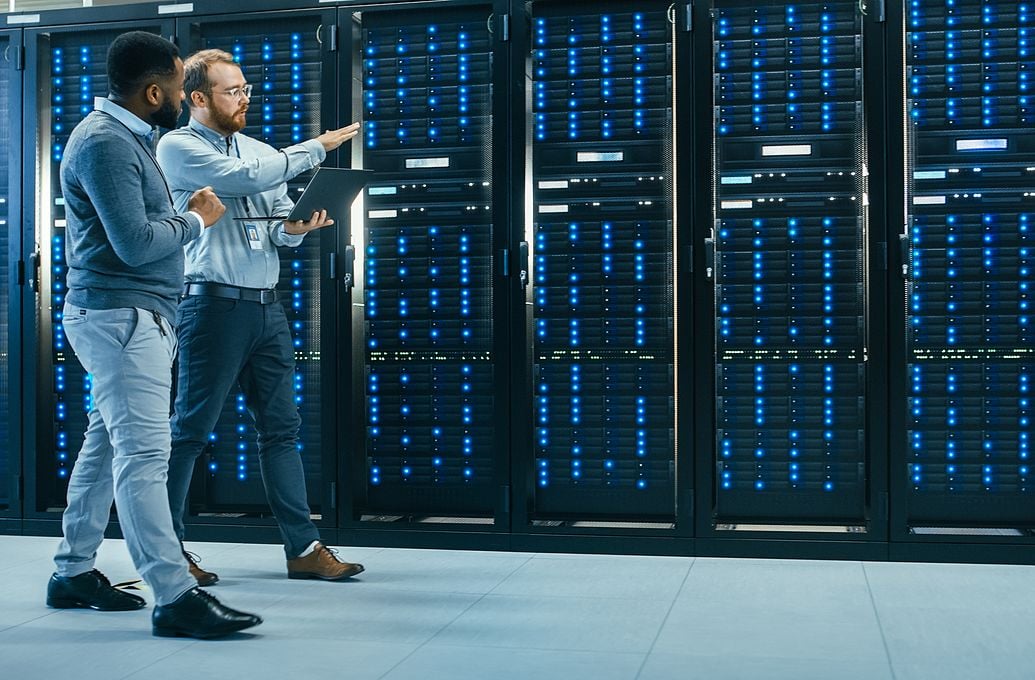 two men in server room holding laptops